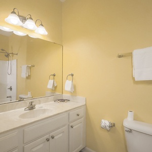 Brightly painted guest bathroom featuring a large mirror, a tub/shower combo, and a spacious countertop with ample storage