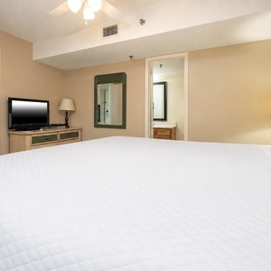 Spacious bedroom features a king bed, a flat-screen TV, and a dresser, with soft lighting creating a relaxing atmosphere