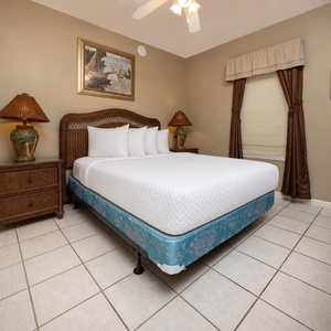 This guest bedroom features a queen bed with soft white linens, wicker furniture, and warm lighting for a relaxing retreat