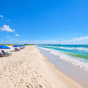 Relax on the soft sand while taking in the stunning beach view and nearby beach chairs under bright blue skies