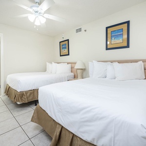 Guest room featuring two double beds, a ceiling fan, and beach-themed artwork, creating a relaxing atmosphere