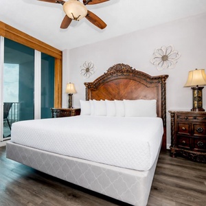 The master bedroom features a king-sized bed, elegant wooden furnishings, and a stunning beachfront view from the balcony