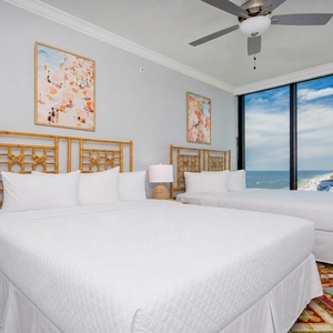 Relax in this inviting guest bedroom featuring two queen beds, vibrant art, and expansive windows with coastal views