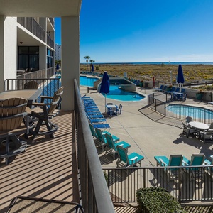 Balcony with outdoor dining set overlooks the pool area, featuring lounge chairs and a view of the beach beyond