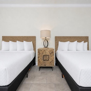 Rest comfortably in this stylish guest room featuring two queen beds, soft lighting, and a bedside lamp