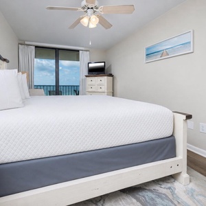 Cozy master bedroom featuring a plush king bed, a flat-screen TV, and a balcony with a captivating coastal view