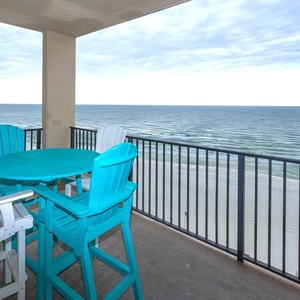 Bright turquoise seating surrounds a table on the balcony, offering a relaxing spot to enjoy views of the beach and waves