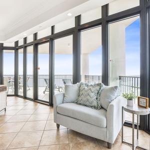The living area features a cozy light blue chair, large windows offering a stunning beach view, and stylish decor