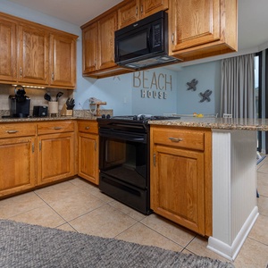 The kitchen features warm wood cabinetry, a black refrigerator, and a breakfast bar, with a view of the outdoor patio beyond