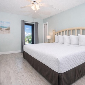 The master bedroom features a large bed, soft bedding, and a view of lush greenery through the window