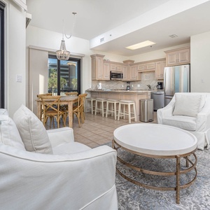 Living area featuring white seating, a round coffee table, and a dining space adjacent to a kitchen with light cabinetry