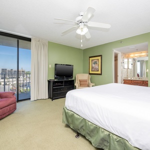 Master bedroom featuring a king bed, a plush armchair, a TV, and a sliding door leading to the balcony with a view