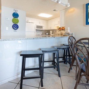 This kitchen features sleek white cabinetry, a granite countertop, and a cozy dining area with colorful seating