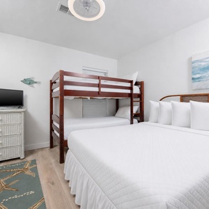 The guest bedroom features a bunk bed and a queen bed, complemented by a TV and beach-themed decor for a relaxing stay