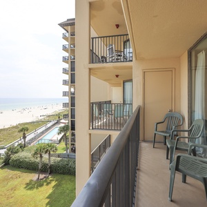 The balcony features green chairs with a view of the beach and a pool area, inviting relaxation and enjoyment of the scenery