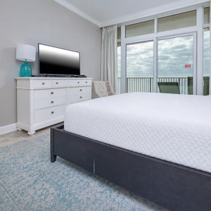 Comfortable master bedroom featuring a king bed, large TV, and beachfront balcony access