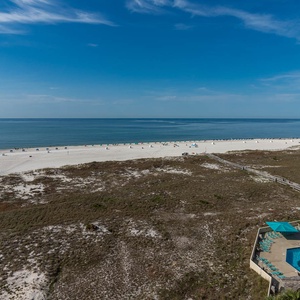 Stunning beach front view reveals white sand, turquoise waters, and a pool area with lounge chairs under a clear blue sky