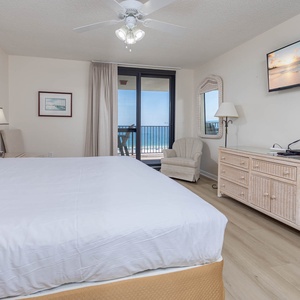 Bright master bedroom featuring a king bed, a cozy seating area, and a balcony with views of the tranquil gulf waters