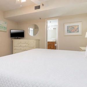Bedroom featuring a large king bed with white linens, a TV, and a doorway leading to a bathroom with towels visible