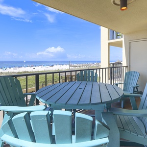 A turquoise table and chairs on the balcony overlook a beach with white sand and colorful umbrellas under a clear blue sky
