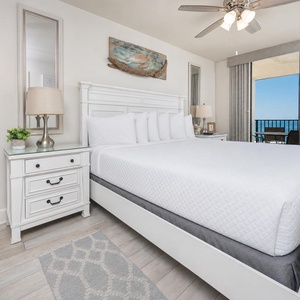 Master suite featuring a king bed, stylish nightstands, and a balcony view overlooking the beach