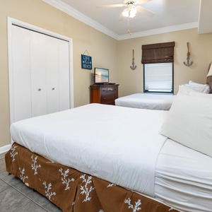 A cozy guest bedroom features two full beds, white linens, a dresser, and beach-themed decor, creating a relaxed atmosphere