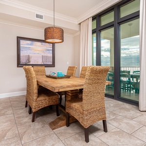 This dining area features a rustic wooden table with woven chairs, with stunning beachfront views through large windows