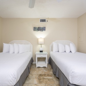 Bright guest bedroom featuring two double beds, a bedside table, and cheerful artwork, creating a welcoming atmosphere