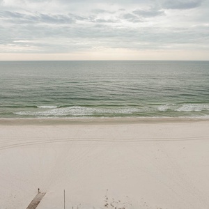 This serene beachfront view showcases soft white sand and gentle waves, perfect for a relaxing getaway