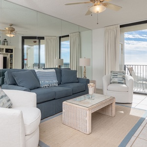 Cozy seating area features a blue sofa with queen sleeper, a glass-top coffee table, and expansive views of the beach