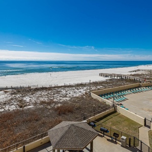 Serene beachfront view with white sand, a sparkling pool area, and a clear blue sky above