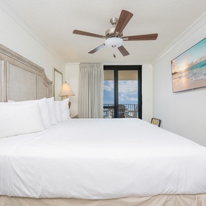 Spacious master bedroom features a king bed, a mounted TV, and a balcony with views of the gulf, creating a serene retreat