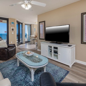 Bright living area features a comfortable leather sofa, large TV, and stunning gulf views through expansive glass doors