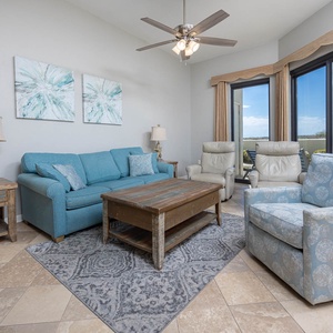 Living area features a blue sofa with queen sleeper, armchairs, and large windows offering a view of the outdoor patio