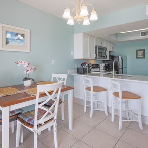 This bright kitchen features stainless appliances, granite countertops, and a cozy dining area with a charming beach view