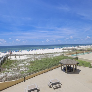 Balcony view showcasing a vibrant beach with colorful umbrellas, the pool area, and a gazebo, all under a clear blue sky