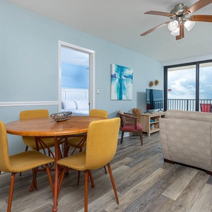 This cozy living area features a stylish round dining table, a TV, and a stunning beachfront view through large windows