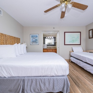 The master suite features a king bed with a woven headboard, a twin trundle bed, and a flat-screen TV mounted on the wall
