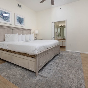 Spacious master bedroom features a king bed, a stylish dresser, and an en-suite bathroom visible through the door