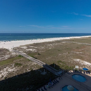 Expansive view of the beach with white sand, lounge chairs, and a pool area, inviting relaxation under a clear blue sky