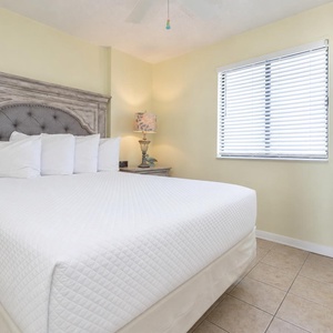 This cozy bedroom features a queen bed with decorative pillows, a charming lamp, and a cheerful beach-themed wall art