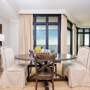 This elegant dining area features a round table with decorative accents and offers a view through large balcony windows