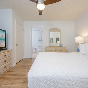 A cozy guest bedroom features a queen bed, a dresser with a mirror, a TV, and an adjoining bathroom for added convenience