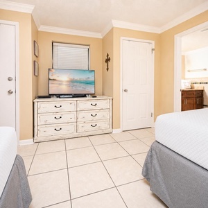 Guest bedroom featuring two double beds, a TV on a dresser, and a doorway leading to a bathroom with a modern vanity