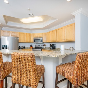 Bright kitchen with granite countertops, stainless appliances, and stylish woven barstools for casual dining