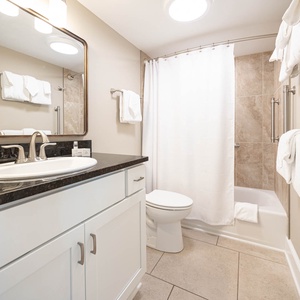 This bathroom features a sleek dark countertop, a spacious shower area, and fresh white towels for a refreshing experience