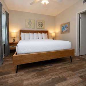 Cozy guest room featuring a king bed, soft lighting, and beach-themed artwork, creating a relaxing atmosphere for vacationers