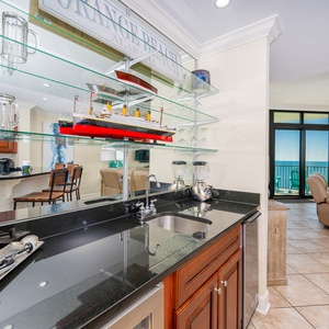 This elegant wet bar features a sleek black countertop, glass shelves, and a blender for creating your favorite cocktail
