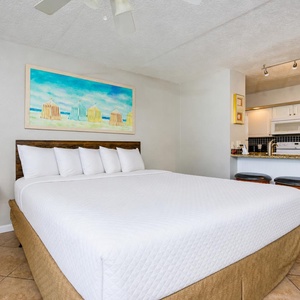 Cozy studio featuring a king bed, vibrant beach-themed artwork, and a convenient kitchen with bar seating