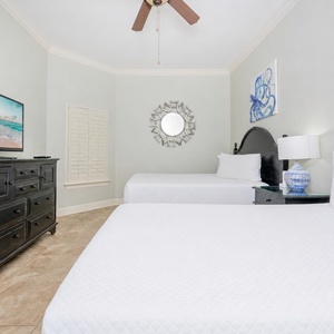 Bright and inviting guest bedroom featuring two queen beds, a flat-screen TV, and coastal-inspired decor
